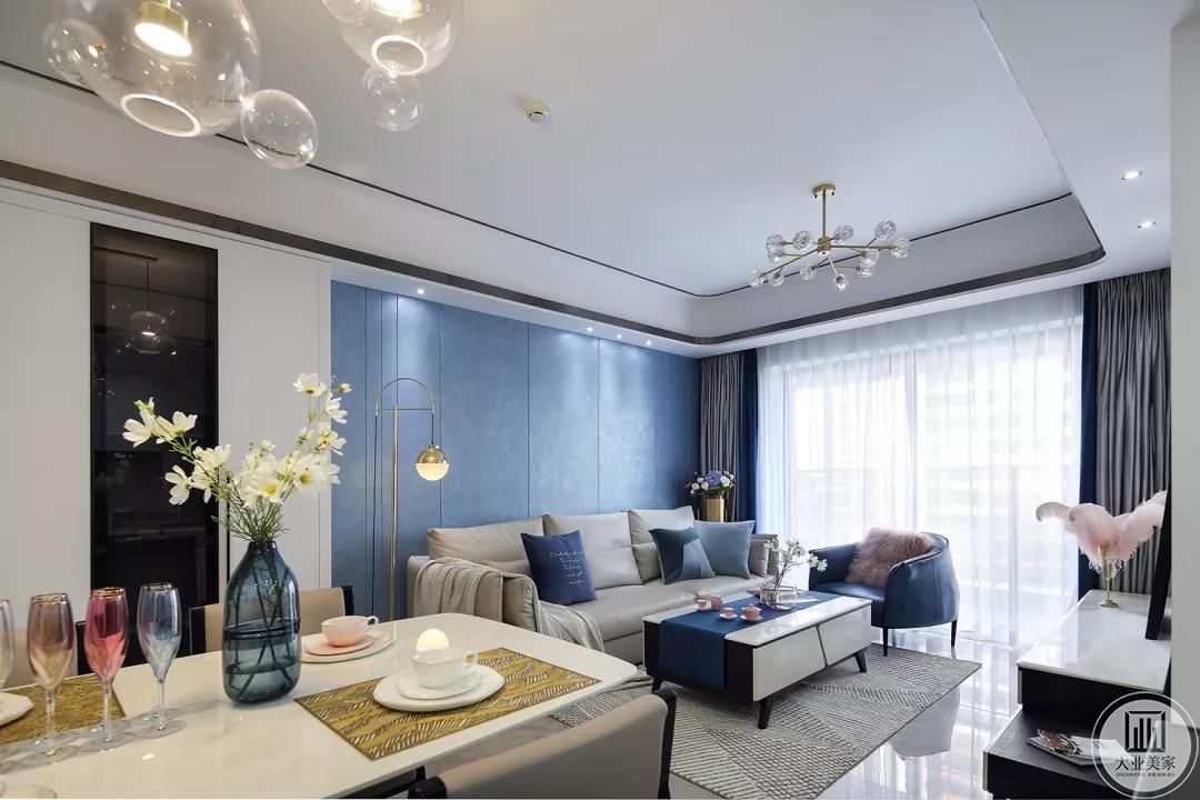 米灰色皮质沙发，背靠静谧蓝色系护墙板沙发背景墙，再以蓝色系抱枕、单人皮沙发和茶几盖布产生色彩共鸣。